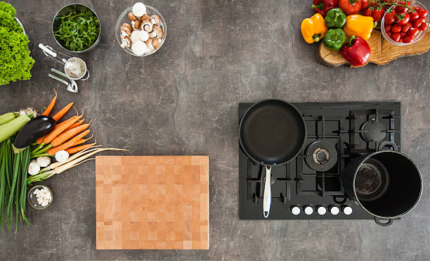 Overhead view of kitchen counter with stove Overhead view of kitchen counter, stove with empty cooking and frying pan, vegetables and various cooking ingredients. burner stove top stock pictures, royalty-free photos & images