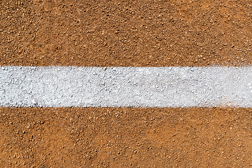 An overhead view of a painted white Foul Line on dirt of a baseball field infield diamond. Sometimes this can be referred to as a Fair Line as it is in Fair Territory and the area from the edge of the line is Foul Territory.