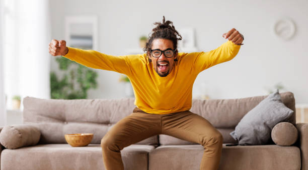 Overjoyed excited young african american man celebrating goal while watching football match on tv stock photo
