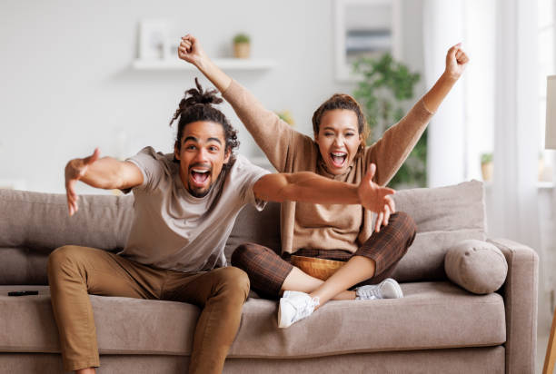 Overjoyed young african american couple celebrating goal while watching football match together stock photo