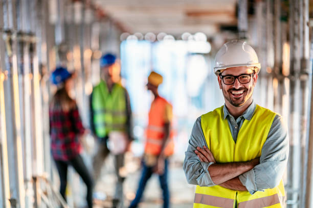 Photo of business people group on meeting and presentation in bright modern office with construction engineer architect and worker looking building model. Front view of smiling architect in helmet against his three colleagues.