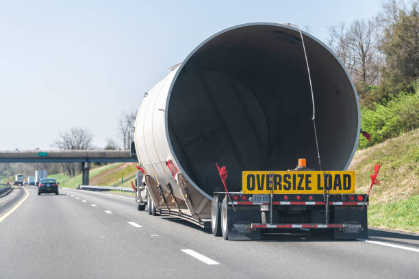Oversize load hauler truck hauling concrete pipe tube on interstate highway in Virginia with yellow warning signs and red flags Woodstock, USA - April 18, 2018: Oversize load hauler truck trailer vehicle hauling concrete pipe tube on interstate highway road in Virginia with yellow warning signs and red flags oversized object stock pictures, royalty-free photos & images