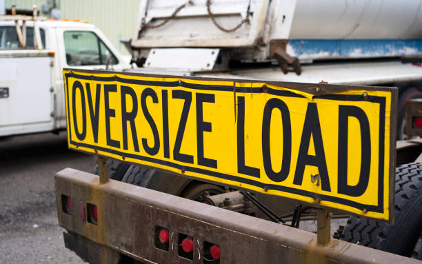 Oversize load sign on the back of big rig semi truck tractor on the parking lot Black on yellow oversize load sign Installed on the back of big rig semi truck tractor with heavy metal bumper for safety moving stand on the parking lot awaiting for the next oversized cargo oversized object stock pictures, royalty-free photos & images