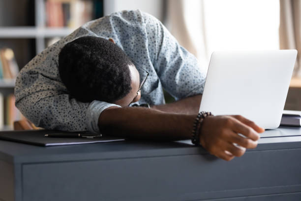 Overworked African employee sleeps at workplace desk African guy student fall asleep on desk due to long time study prepare for university exams. Overworked employee sleeps at workplace table near opened laptop, fatigue need rest, lack of energy concept wasting time stock pictures, royalty-free photos & images