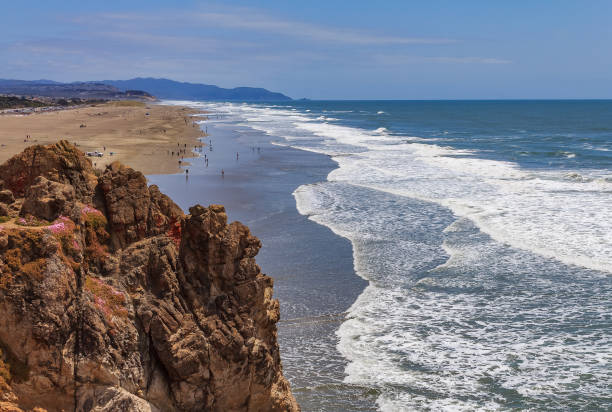Photo of Pacific Ocean waves crashing on the sandy Ocean Beach in San Francisco with a rugged cliff in the background