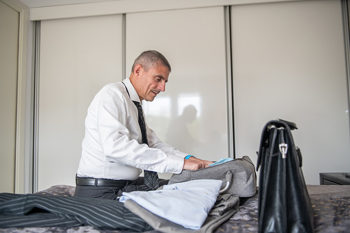 Packing for a trip. \nPortrait of  businessman packing in his hotel .