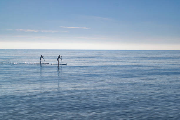 Paddleboarders on flat calm seas stock photo