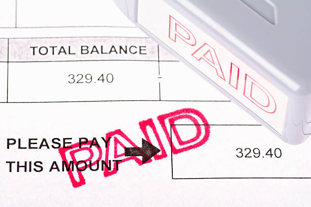 Paid Bill Copy of a billing statement with a dollar amount balance. The word 'PAID' is stamped on the bill and the rubber stamper is off to the side. paid stamp stock pictures, royalty-free photos & images
