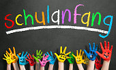bemalte Kinderhände und das Wort "erster Schultag" auf Deutsch auf einer Tafel