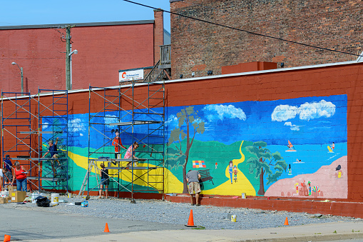 Saint John, NB, Canada - July 30, 2015: Volunteers paint a mural on the side of a building as part of the Marigolds and Murals Project.