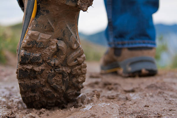 a pair of muddy hiking boots in the mud - muddy shoes stockfoto's en -beelden