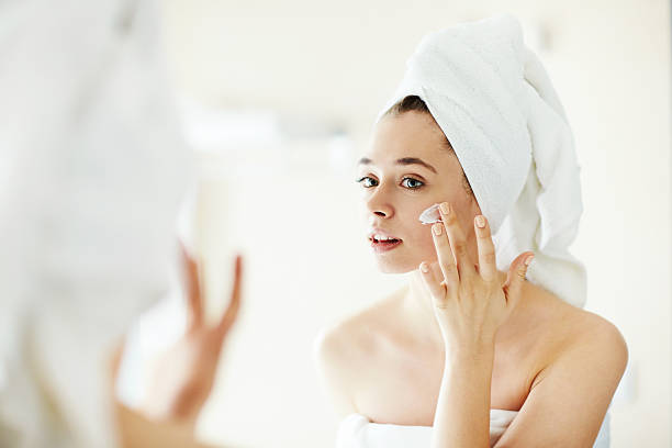 Pampering cream Pretty girl applying moisturizing cream in front of mirror body care and beauty stock pictures, royalty-free photos & images