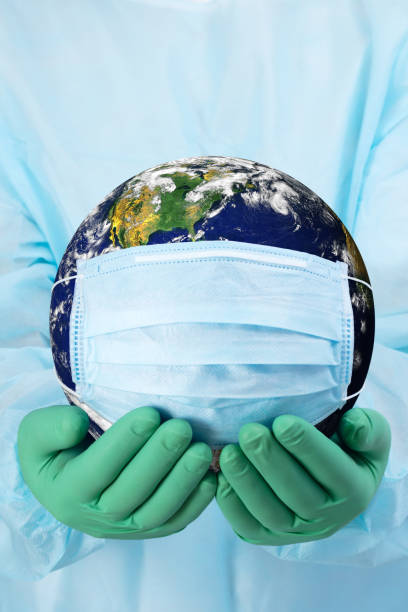 Pandemic concept - doctor's hands in gloves holding the planet Earth in a medical mask stock photo
