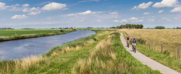 panorama van een paar rijden hun fiets langs de rivier van het reitdiep in groningen, nederland - pensioen nederland stockfoto's en -beelden