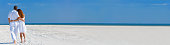 Panorama rear view of man and woman romantic couple on vacation  in white clothes walking on a deserted tropical beach with clear blue sky panoramic web banner.