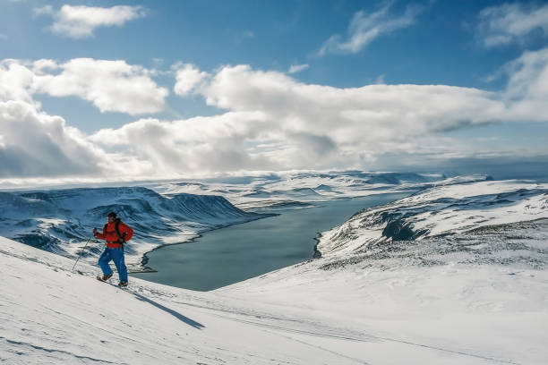 Panorama tall mountaineer dressed in red jacket with trekking poles ascending the top of the snowy mountain in Hornstrandir, Iceland stock photo