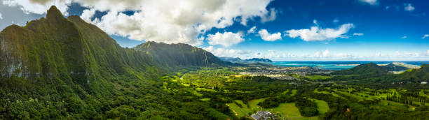 A Panoramic aerial image from the Pali Lookout on the island of Oahu in Hawaii.  With a bright green rainforest, vertical cliffs and vivid blue skies. stock photo
