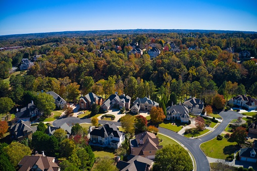 Panoramic aerial view of luxury homes in an upscale neighborhood in the suburbs with beautiful colors of leaves on the trees in the subdivision during fall of 2021.