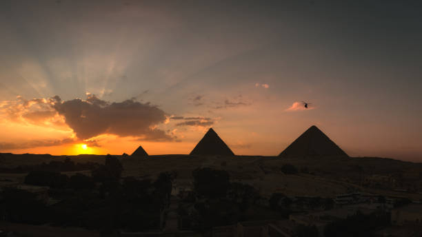 panoramica della sagoma delle tre piramidi di giza (cheope, kefren e micero) al tramonto con raggi di luce dietro le nuvole. il cairo, egitto - cuadrado foto e immagini stock