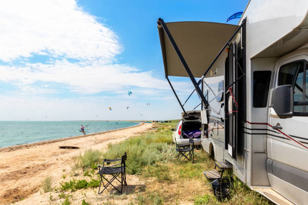 Panoramic view of many surf board kite riders on sand beach watersport spot on bright sunny day against rv camper van vehicle at sea ocean coast at surfing camp. Fun adventure travel sport acitivity stock photo