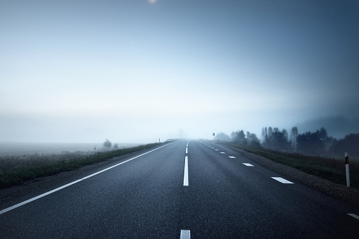 Panoramic view of the empty highway through the fields in a fog at night. Moonlight, clear sky. Sunrise. Europe. Transportation, logistics, travel, road trip, freedom, driving. Rural scene