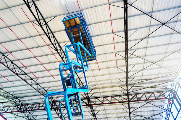 Pantographic mobile crane rises towards the roof of a warehouse under construction stock photo