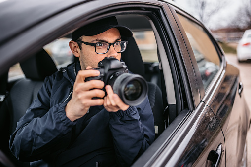 Paparazzi photographer is taking photos through car window. Private detective, undercover agent, plain-clothes police work, paparazzi concepts.