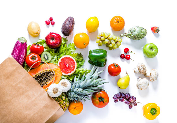 Paper bag full of various kinds of fruits and vegetables on white background Top view of a paper bag full of various kinds of multicolored fruits and vegetables like papaya, tomatoes, red and green apples, carrots, mushrooms, eggplants, pineapple, cherries, lime, garlic, oranges and kiwi. The paper bag is laying at the lower left corner on a white background and the fruits and vegetables are coming out from it.  Studio shot taken with Canon EOS 6D Mark II and Canon EF 24-105 mm f/4L. fruit stock pictures, royalty-free photos & images