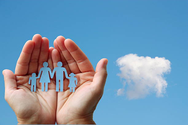 Paper family in hands on blue sky background welfare concept stock photo