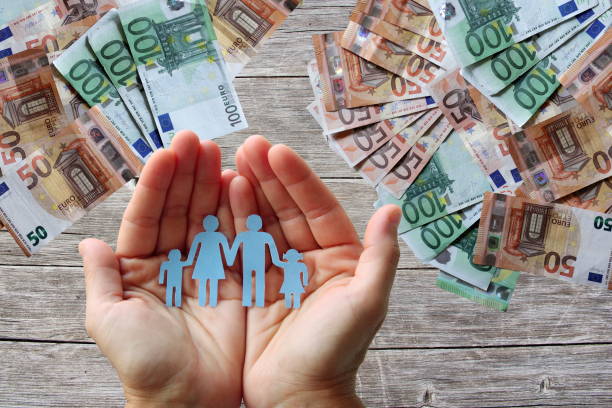 Paper family in hands on wooden background with euro banknotes stock photo