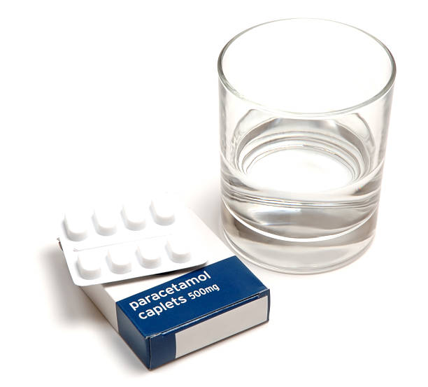 paracetamol pills next to a drinking glass - pijnstiller stockfoto's en -beelden