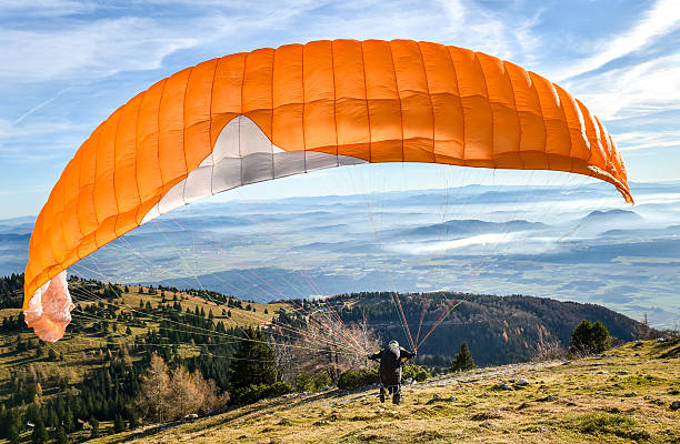 Paraglider is starting  to start his flight. Paraglider is starting  to start his flight. Looking at beautiful valley below with clouds and mist. paragliding stock pictures, royalty-free photos & images