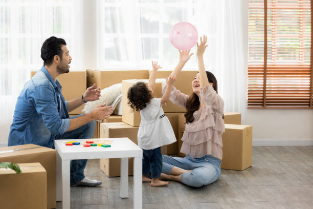 Parents and daughters play with pink balloon sitting on the floor in the living room at home. The family just moved to a new house. Happy moment Multi-ethnic dad mom and child. stock photo