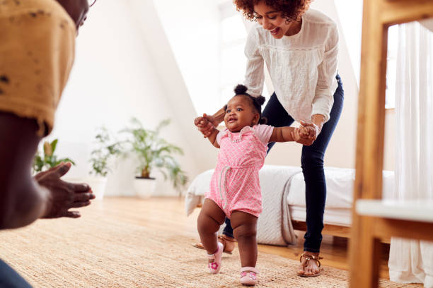 Parents At Home Encouraging Baby Daughter To Take First Steps Parents At Home Encouraging Baby Daughter To Take First Steps walking with moms stock pictures, royalty-free photos & images