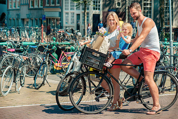 parents on bikes at the streets of amsterdam - zomer nederland stockfoto's en -beelden
