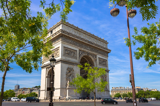 Paris, France - July 13th 2022: Arc de Triomphe in Paris seen through green trees, blue sky background