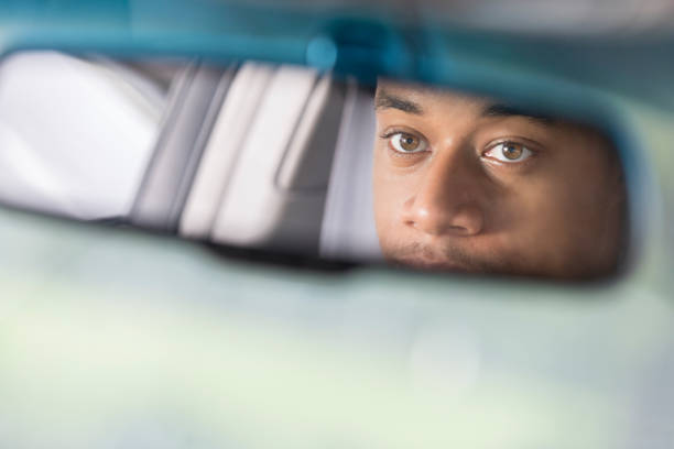 Partial reflection of man looking in rear view mirror A serious man looks in the rear view mirror of a vehicle.  Only his eyes and nose can be seen.  There is copy space. rear view mirror stock pictures, royalty-free photos & images