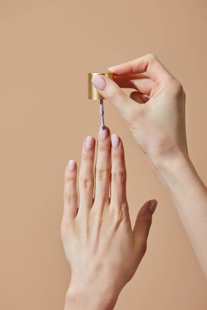 Partial view of woman applying nail polish isolated on beige Partial view of woman applying nail polish isolated on beige painting fingernails stock pictures, royalty-free photos & images