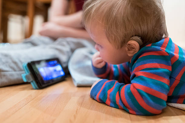 Partially deaf baby watching and listening lullaby on smartphone stock photo