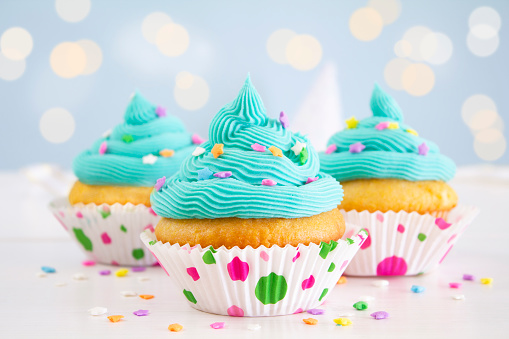 Vanilla and buttercream cupcakes with blue icing and sprinkles, on a blue background.