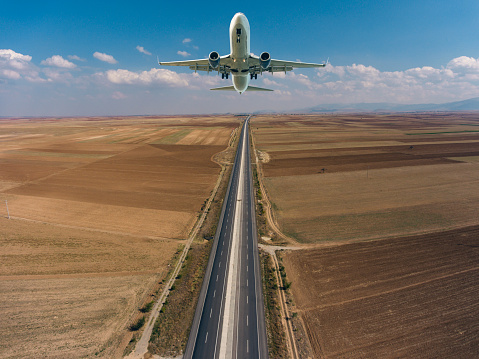 Passenger airplane flying over empty asphalt highway.