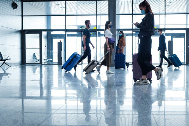 Passengers at the airport with luggage, wearing N95 face masks People traveling by plane during COVID 19, wearing N95 face masks, carrying luggage in airport terminal. airport stock pictures, royalty-free photos & images
