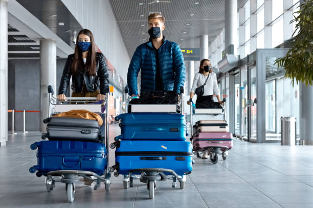 Passengers at the airport with luggage, wearing N95 face masks People traveling by plane during COVID 19, wearing N95 face masks, carrying luggage in airport terminal. luggage cart stock pictures, royalty-free photos & images