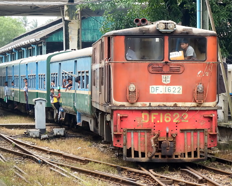 Yangon, Myanmar - August 1st, 2016: A train pulls into Yangon Central railway station with local people hanging on to the exterior and looking out of the train's windows for preparing to disembark.