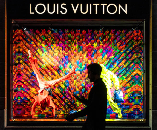 Passing a Louis Vuitton display window Edinburgh, Scotland - A passing man silhouetted by a colourful illuminted display in the shop window of a Louis Vuitton store. brand name stock pictures, royalty-free photos & images
