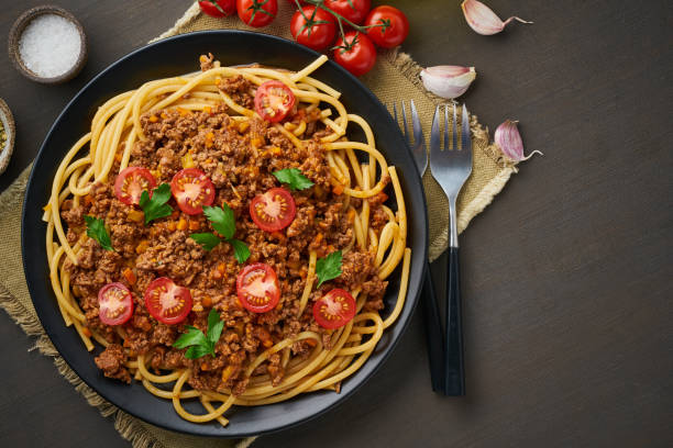 Pasta Bolognese bucatini with mincemeat and tomatoes, dark wooden background, top view, copy space stock photo