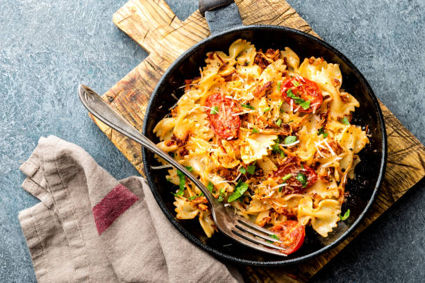 pasta farfalle with roasted meat and tomatoes in a frying pan stock photo