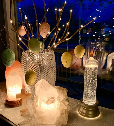 Pastel Easter eggs on lighted branches with carved stone cross, Himalayan salt lamp, clear quartz lamps, and candle