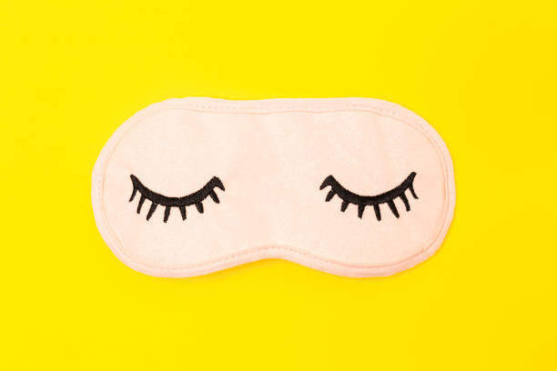 Pastel pink sleep mask with closed eyes embroidered on it with eyelashes on bright yellow neon paper background. Top view, flat lay. Concept of vivid dreams. Accessories for girls and young women. Pastel pink sleep mask with closed eyes embroidered on it with eyelashes on bright yellow neon background. Fashion accessory for sleep. Concept of vivid dreams, accessories for girls and young women eye mask stock pictures, royalty-free photos & images