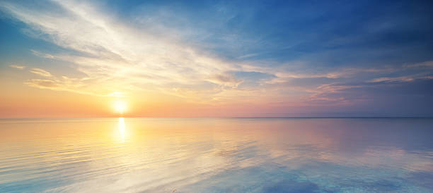 pastel sunset over the ocean in a cloudy sky - panoramisch stockfoto's en -beelden